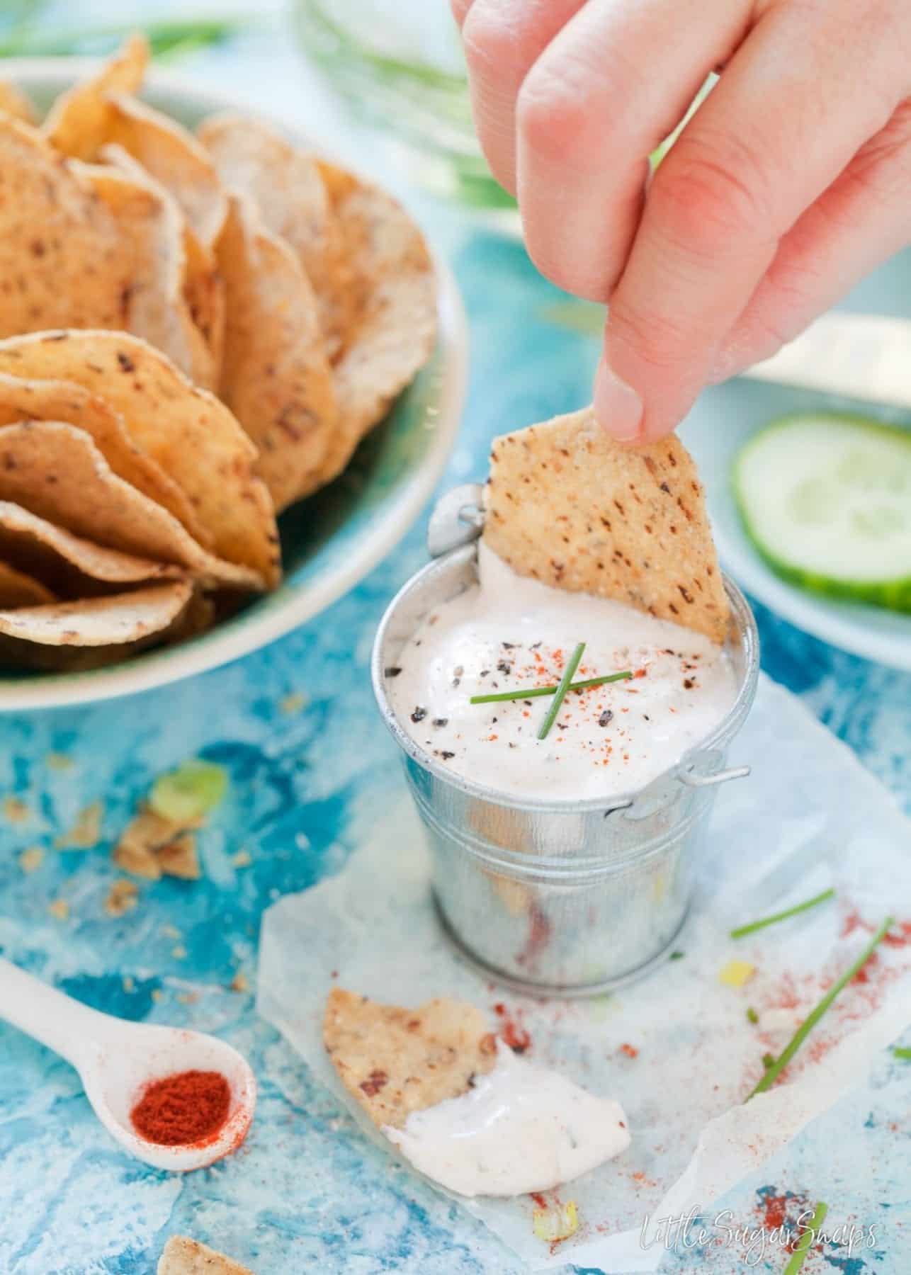 Person dipping a tortilla chip into a small bucket of Paprika Dip.