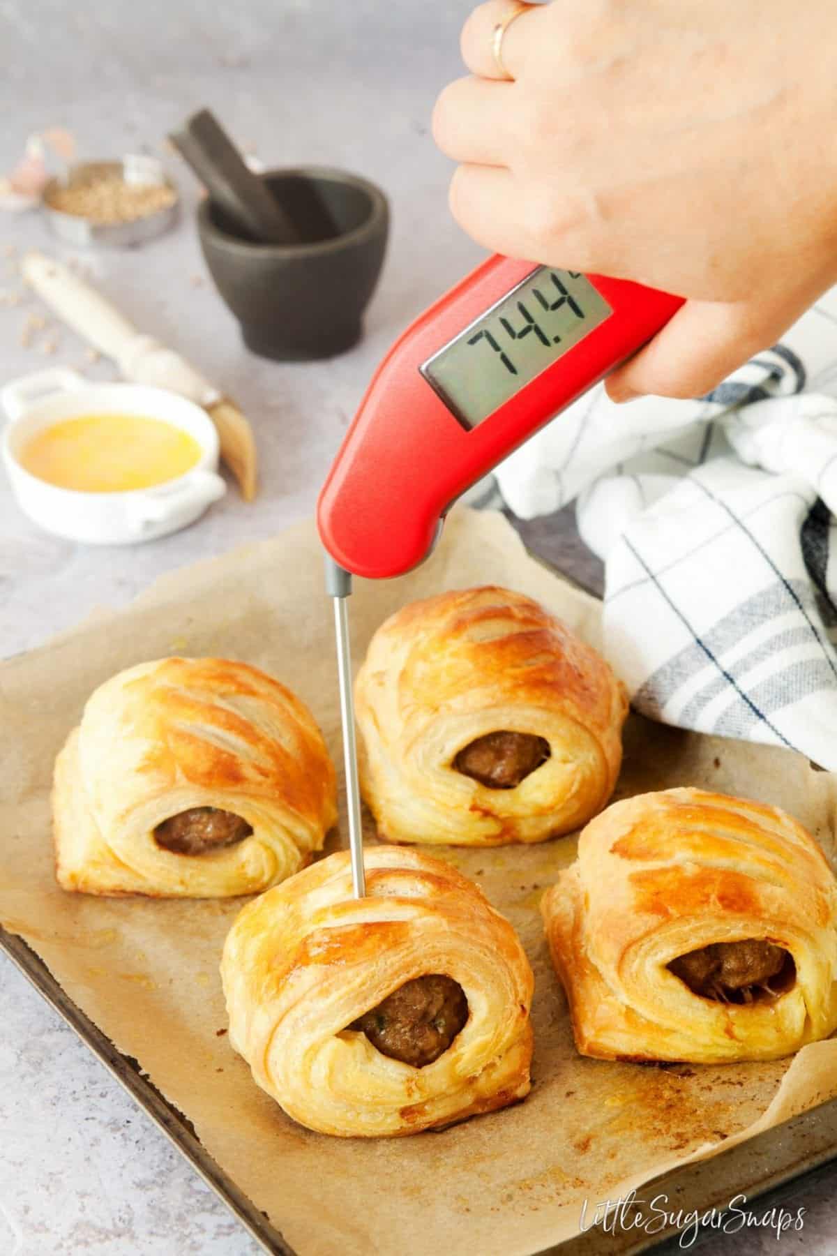 Person using a digital food thermometer to check the temperature of lamb in a pastry roll