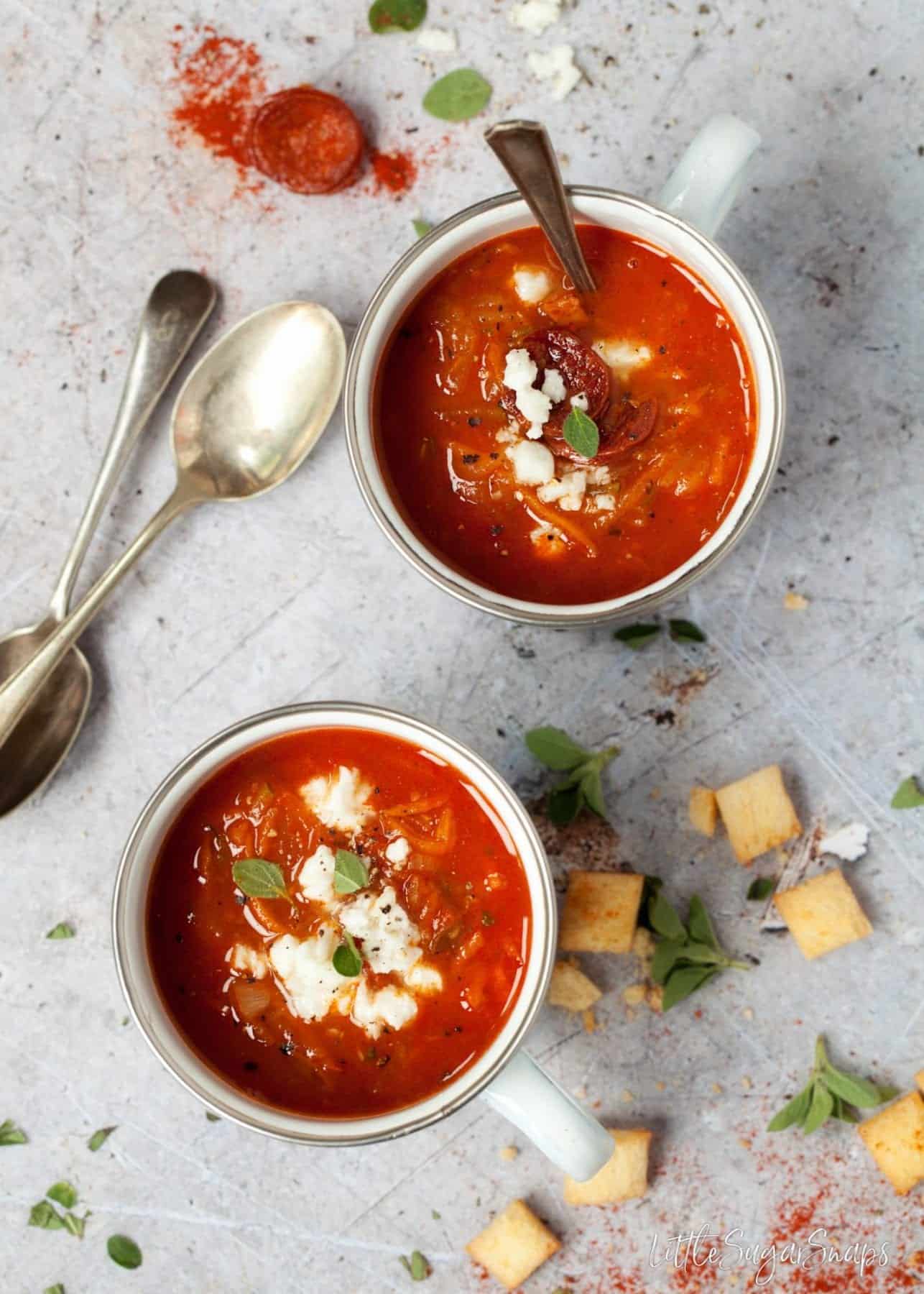 Two mugs of Carrot and courgette soup topped with feta.