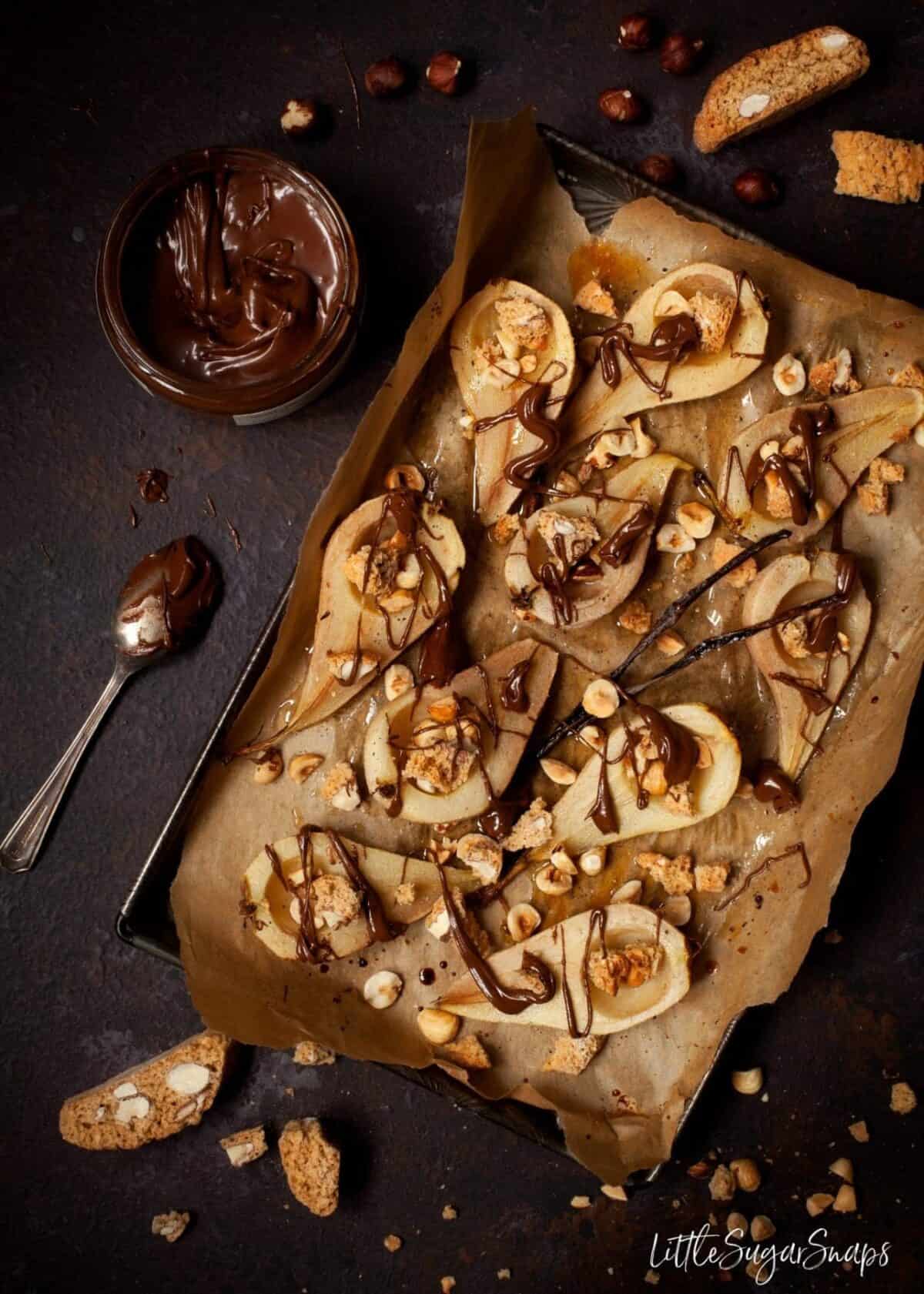 Baked pears on a baking sheet with nuts, chocolate and Italian cookies