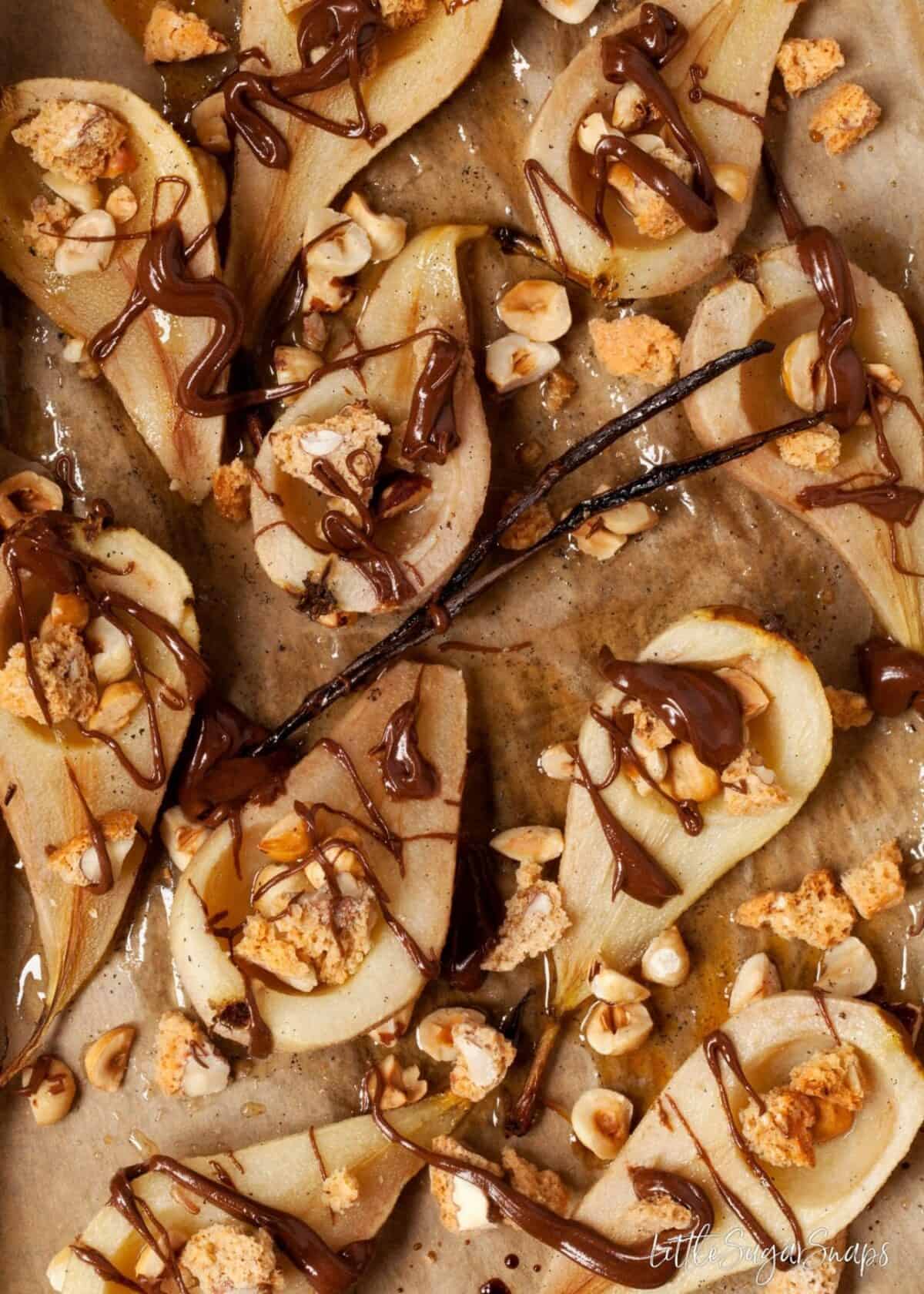 Honey Baked Pears with Chocolate on a baking sheet with hazelnuts and a vanilla pod