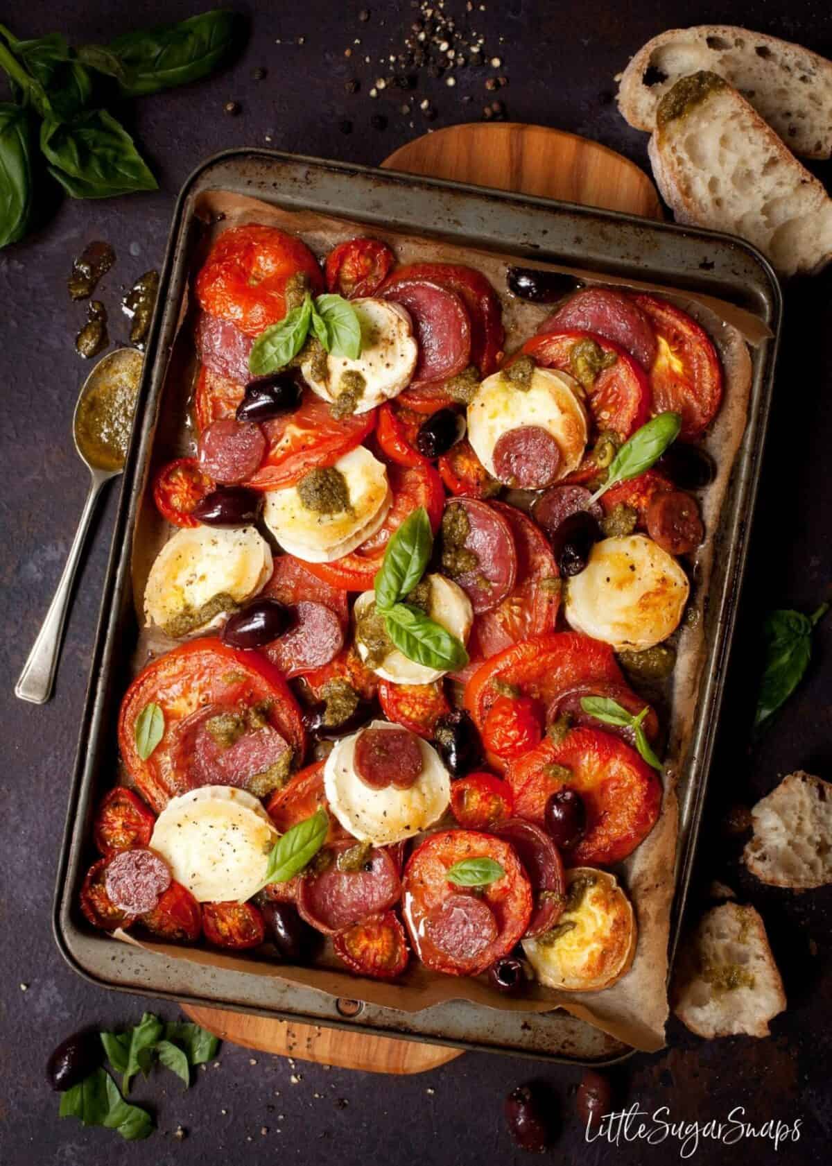 Baked Tomato, Goats Cheese, salami and olives on a baking sheet.