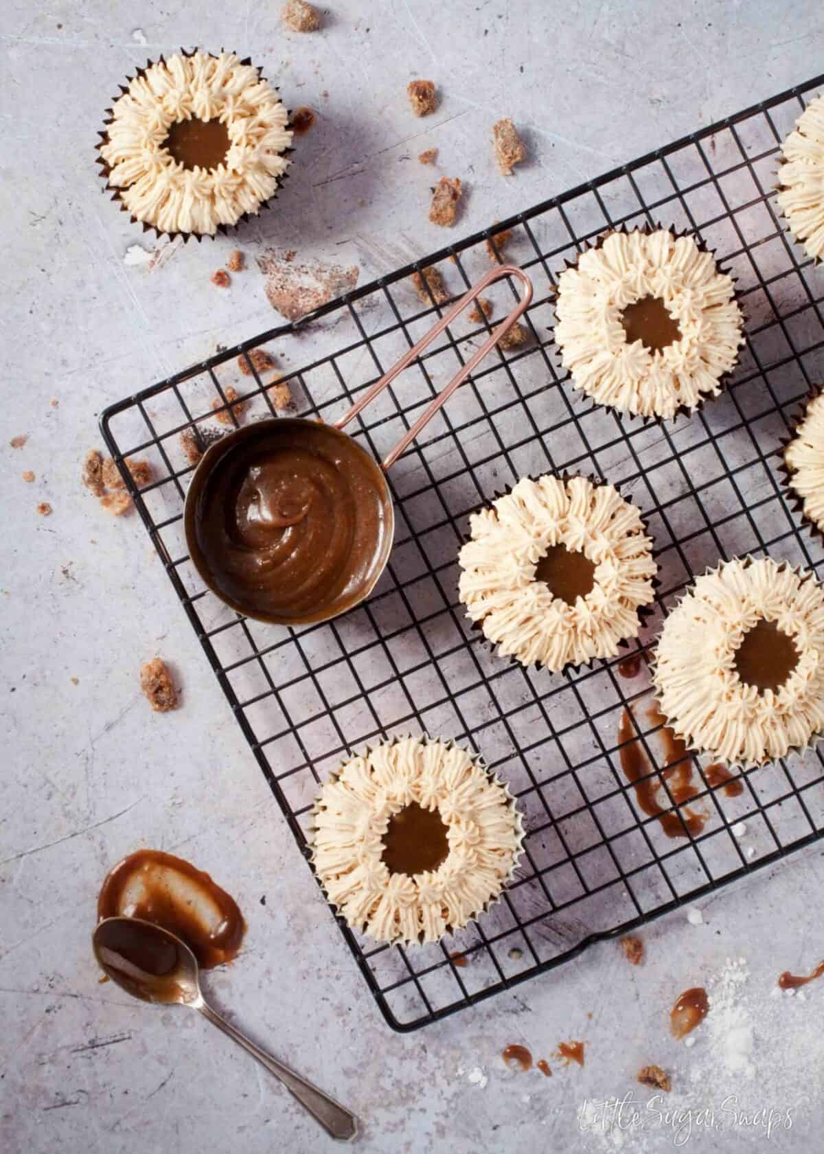 Sticky toffee cupcakes on a cooling rack with piped buttercream and a pot of toffee sauce. 