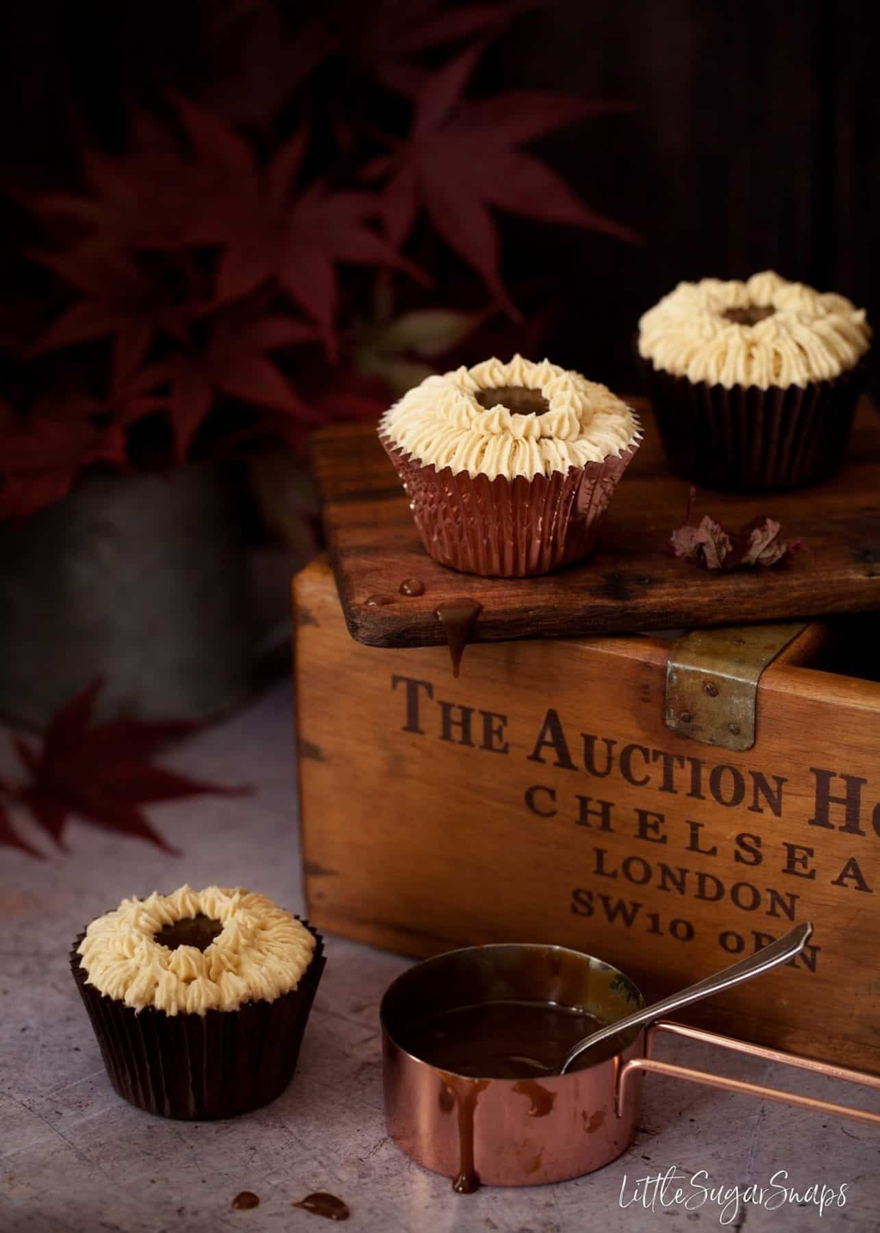 Three small cakes decorated with buttercream and a copper pan of sauce.