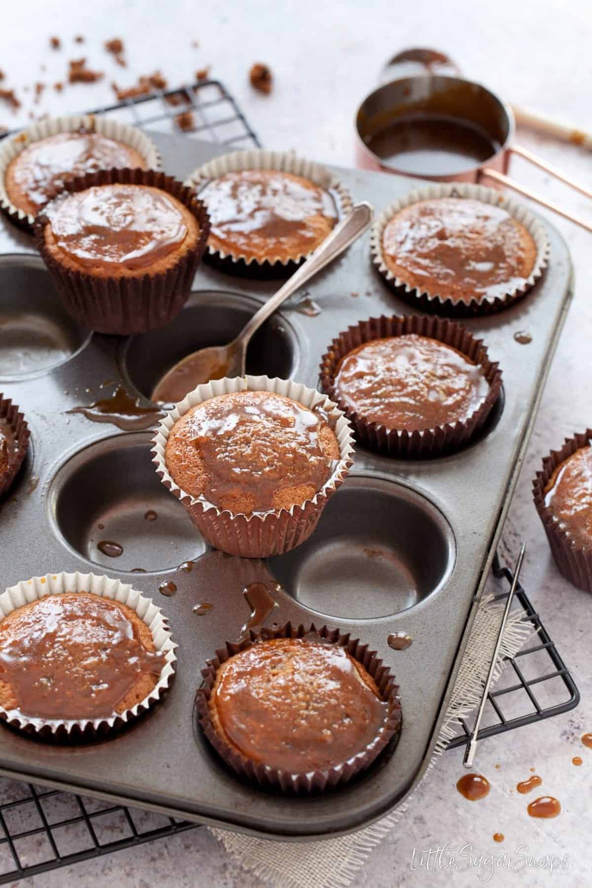 Sticky toffee pudding cupcakes in or on a baking tin being drizzled with sauce.