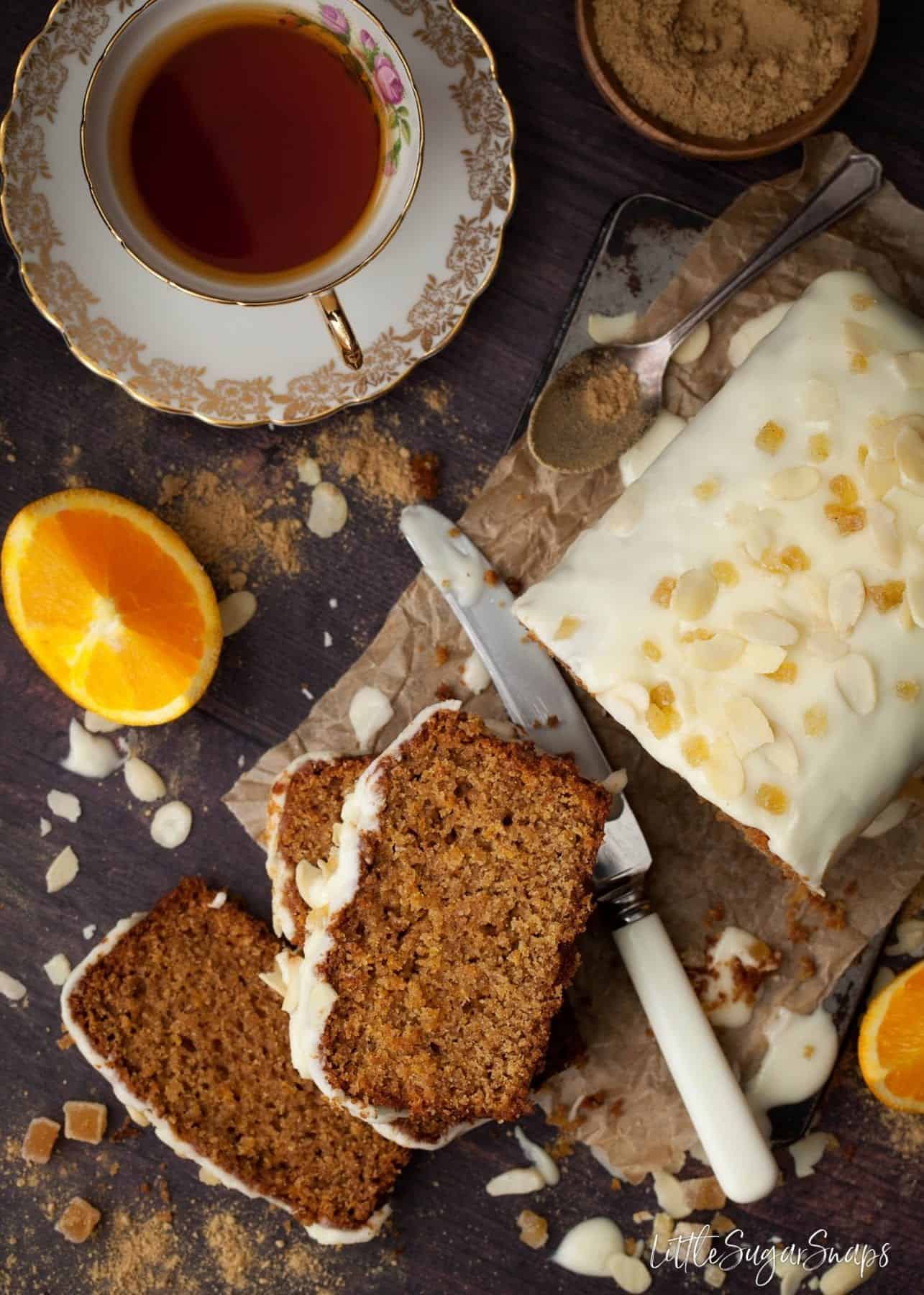 Vegan ginger cake cut into slices with a cup of black tea and orange slices nearby.