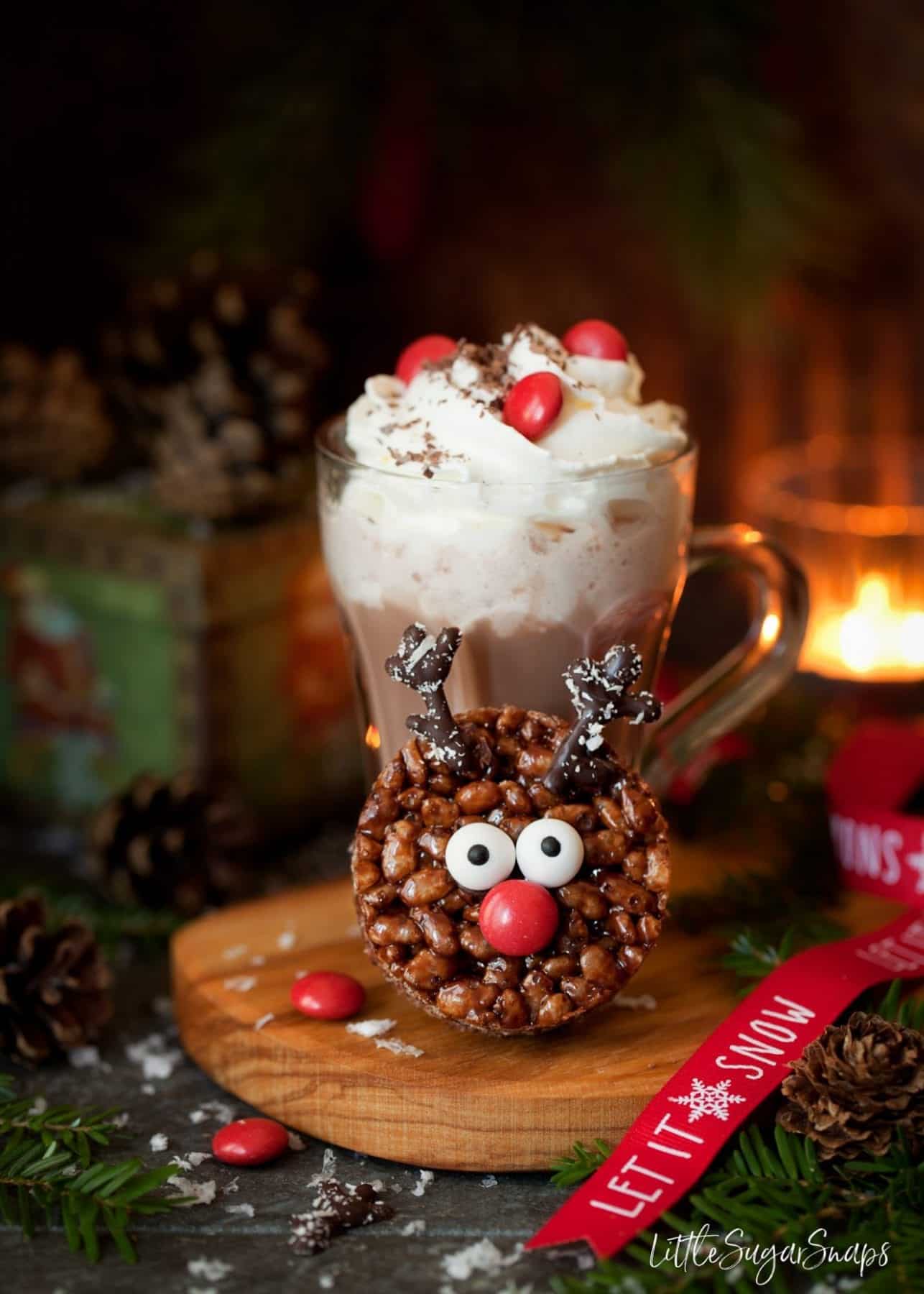 A mug of hot chocolate with a cereal based Christmas themed cookie alongside.