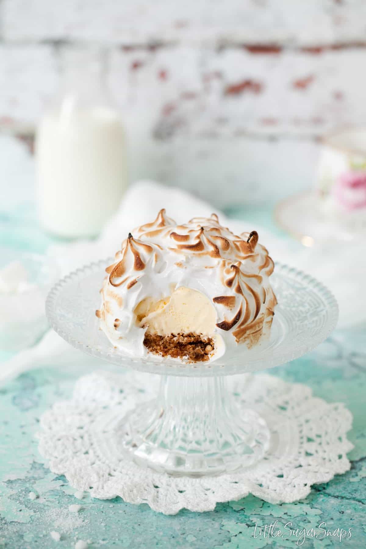 Individual Baked Alaska on a cake stand with a spoonful taken out of it.