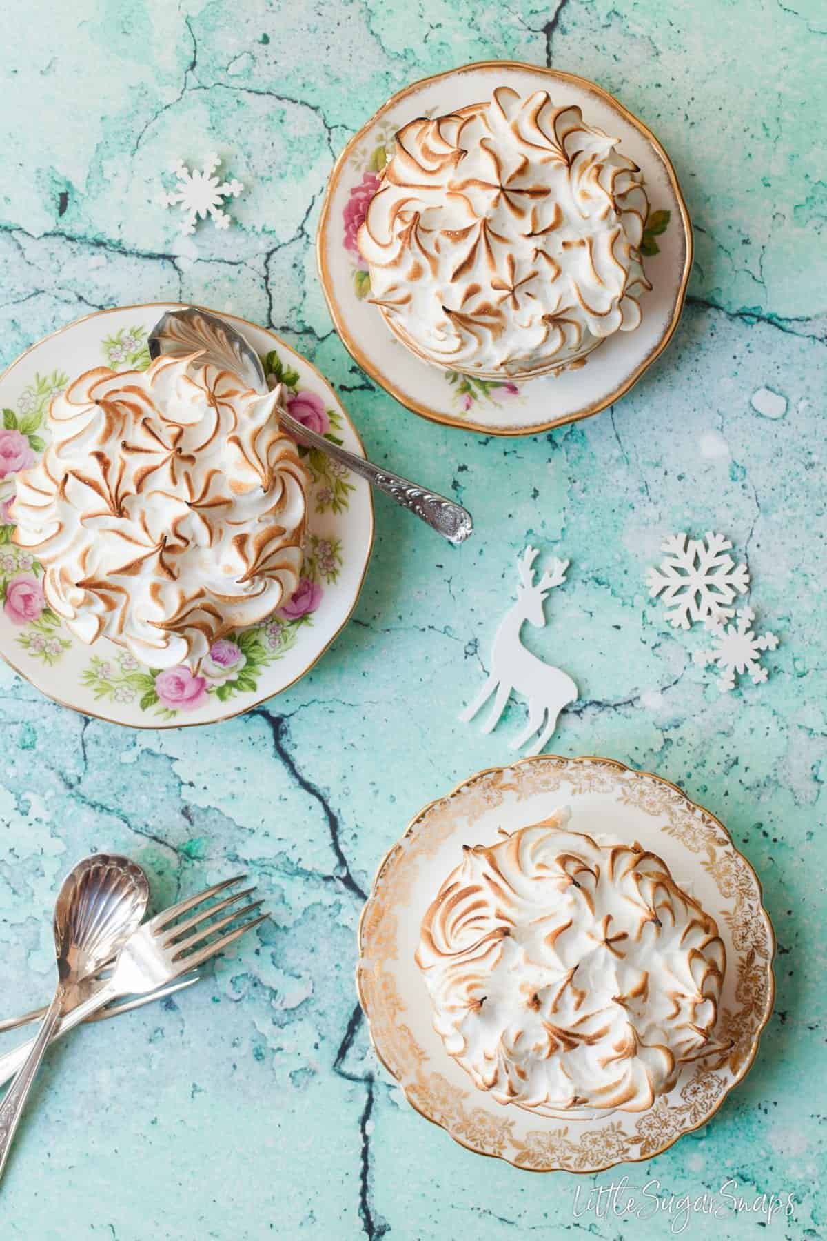 Three individual Baked Alaska desserts on vintage plates.