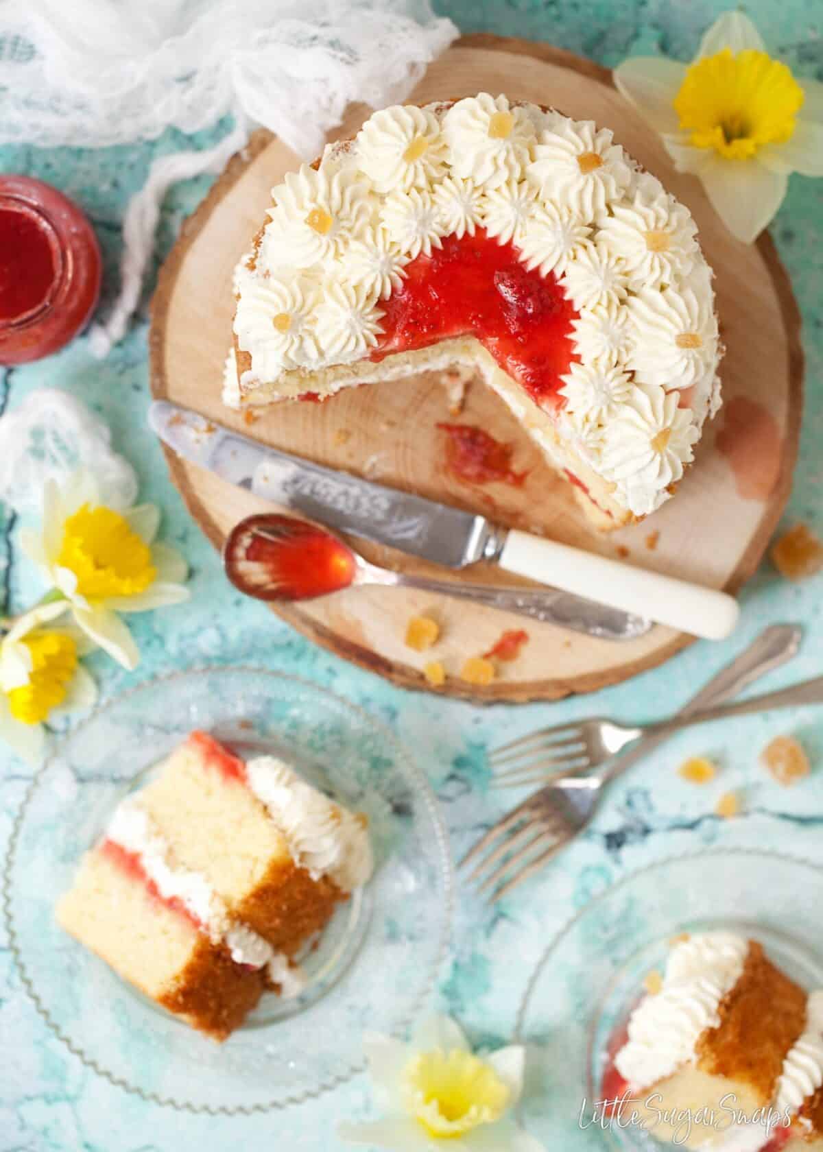 overhead view of a classic sponge cake with strawberry jam and piped cream. Slices have ben cut and are visible on plates at the side