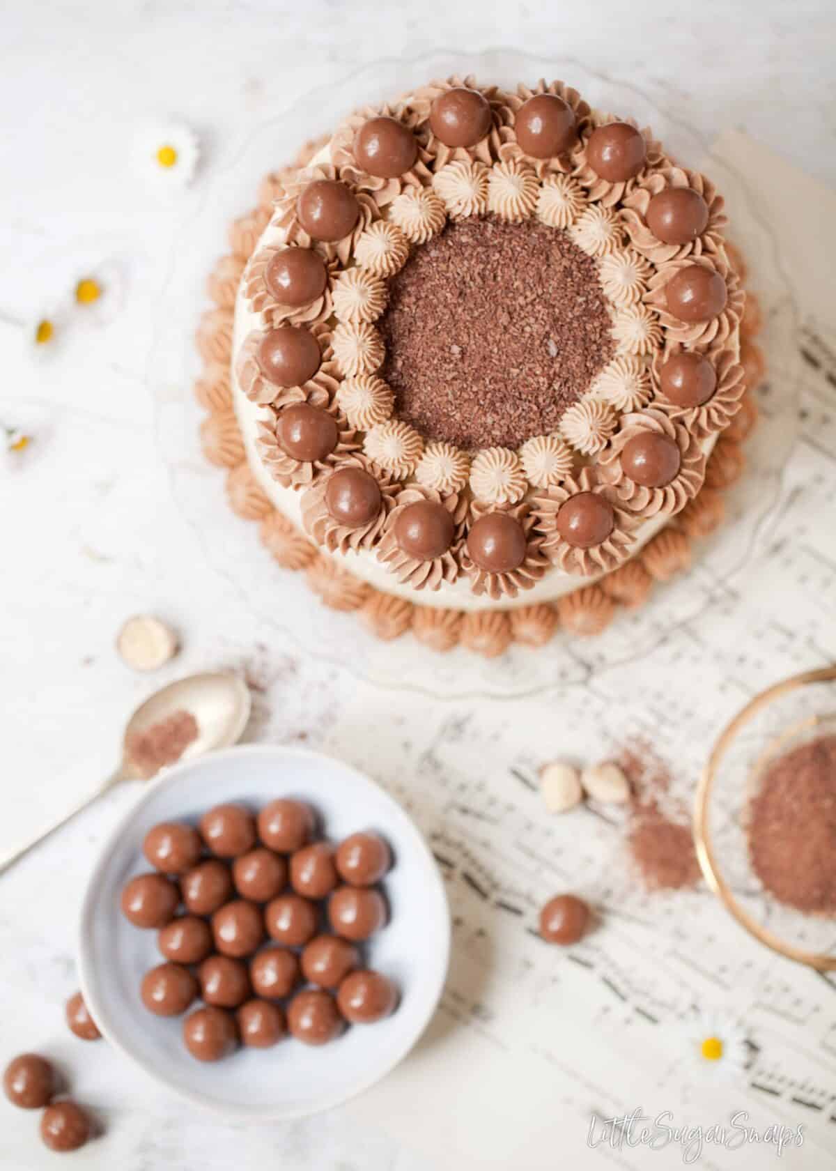 Topdown view of vanilla Malted Milkshake Cake with a bowl of chocolate malt balls (maltersers)