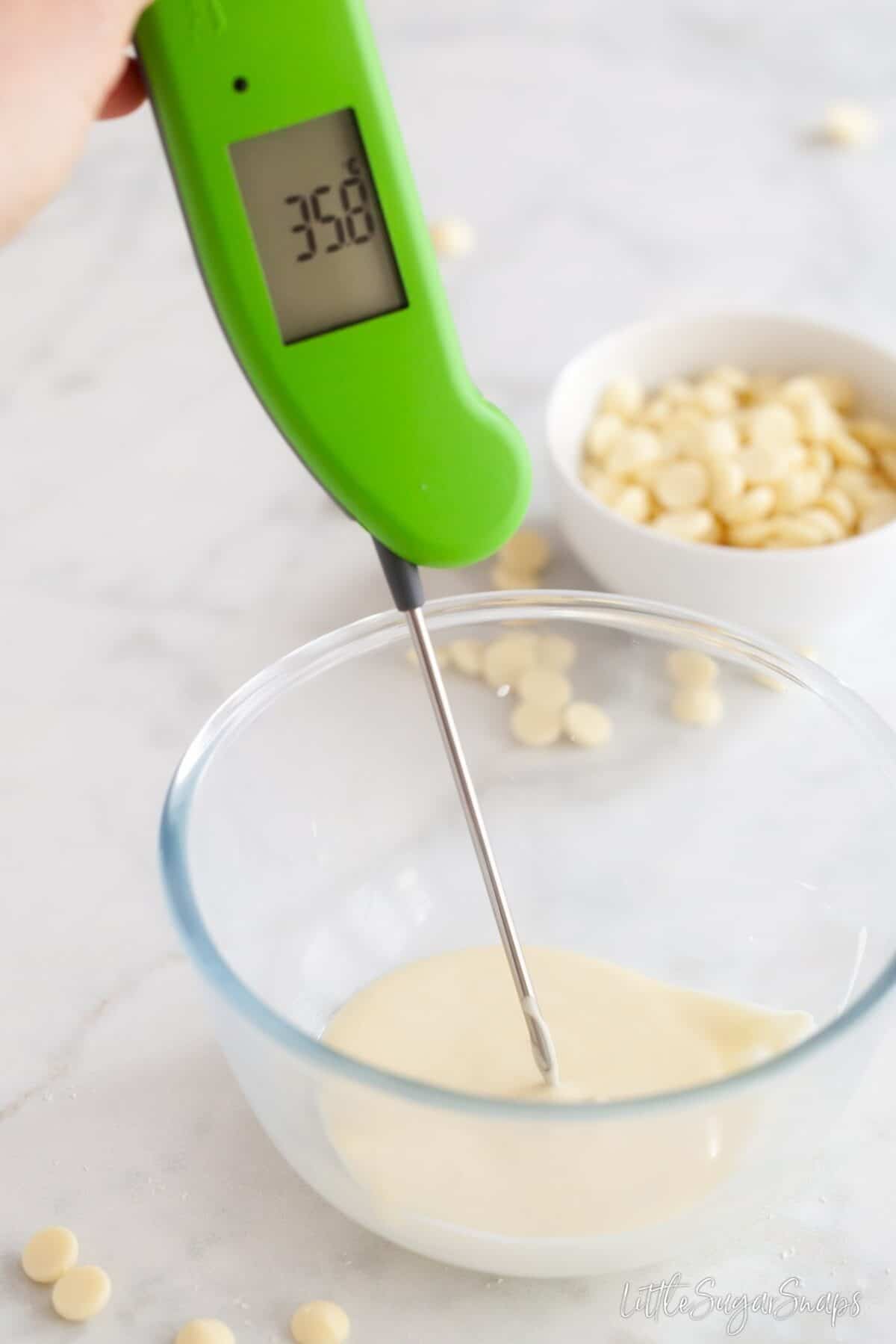 Tempering melted white chocolate using a digital food thermometer to read the temperature.