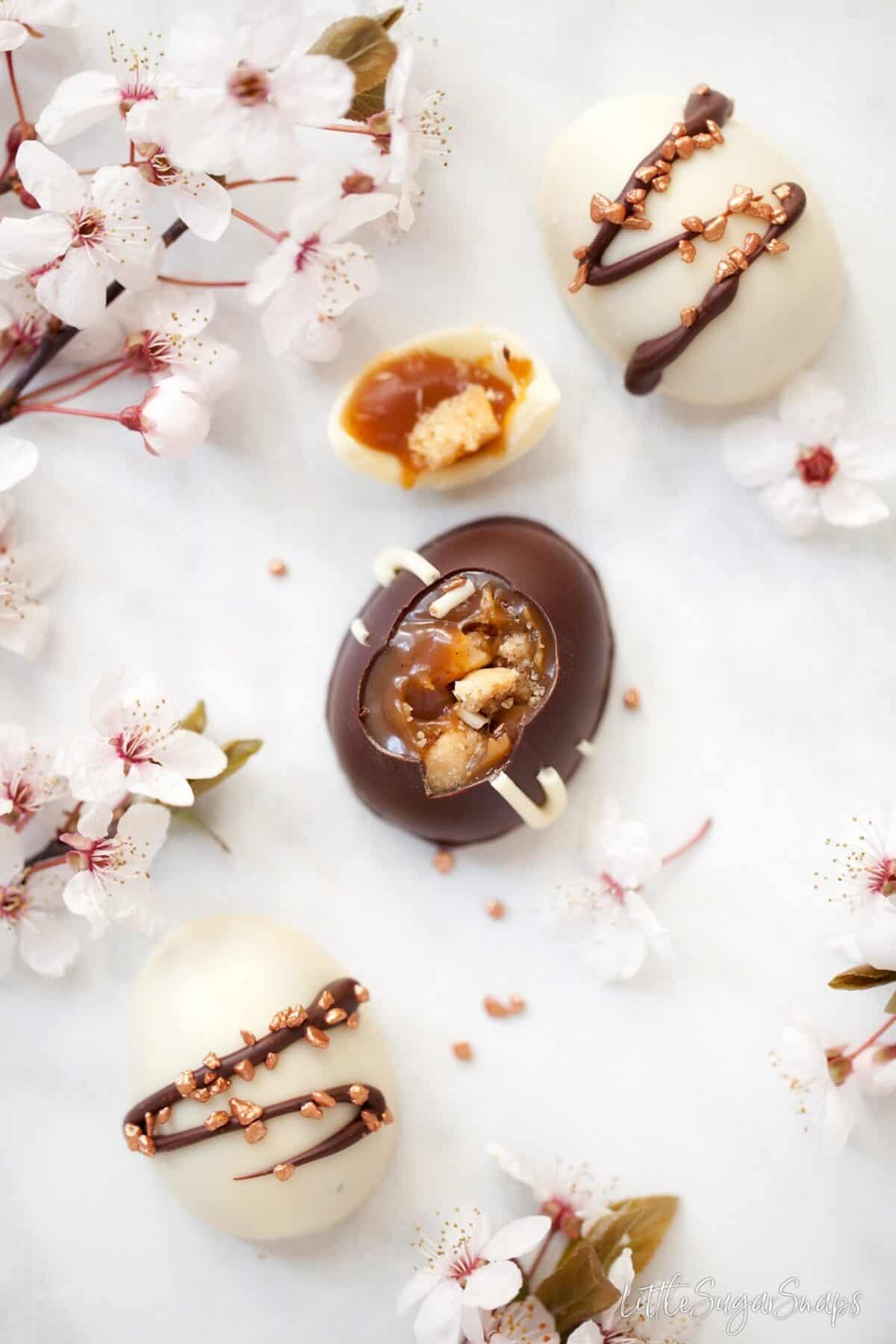 Caramel shortbread chocolate easter eggs on a marble backdrop. One it cut open.