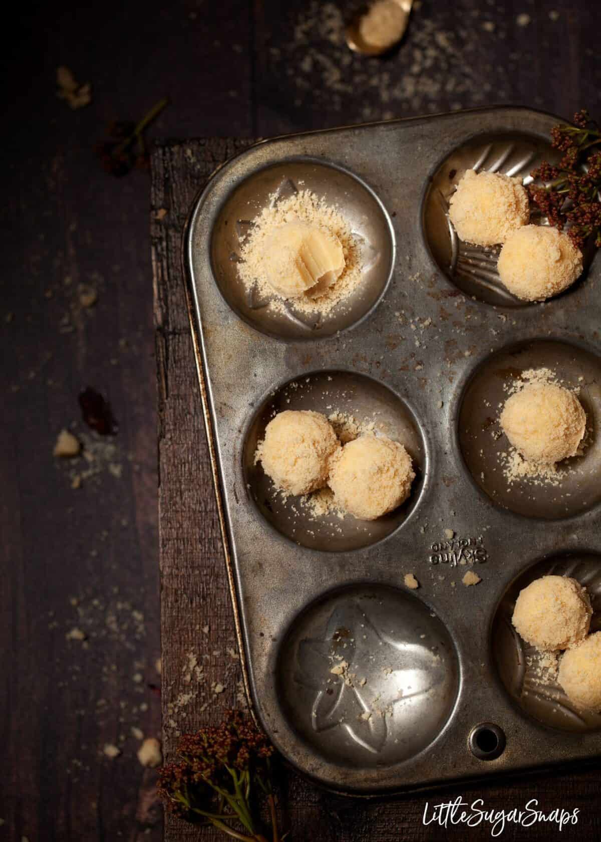 Custard Cream Truffles in a vintage baking tin. One has been bitten into.