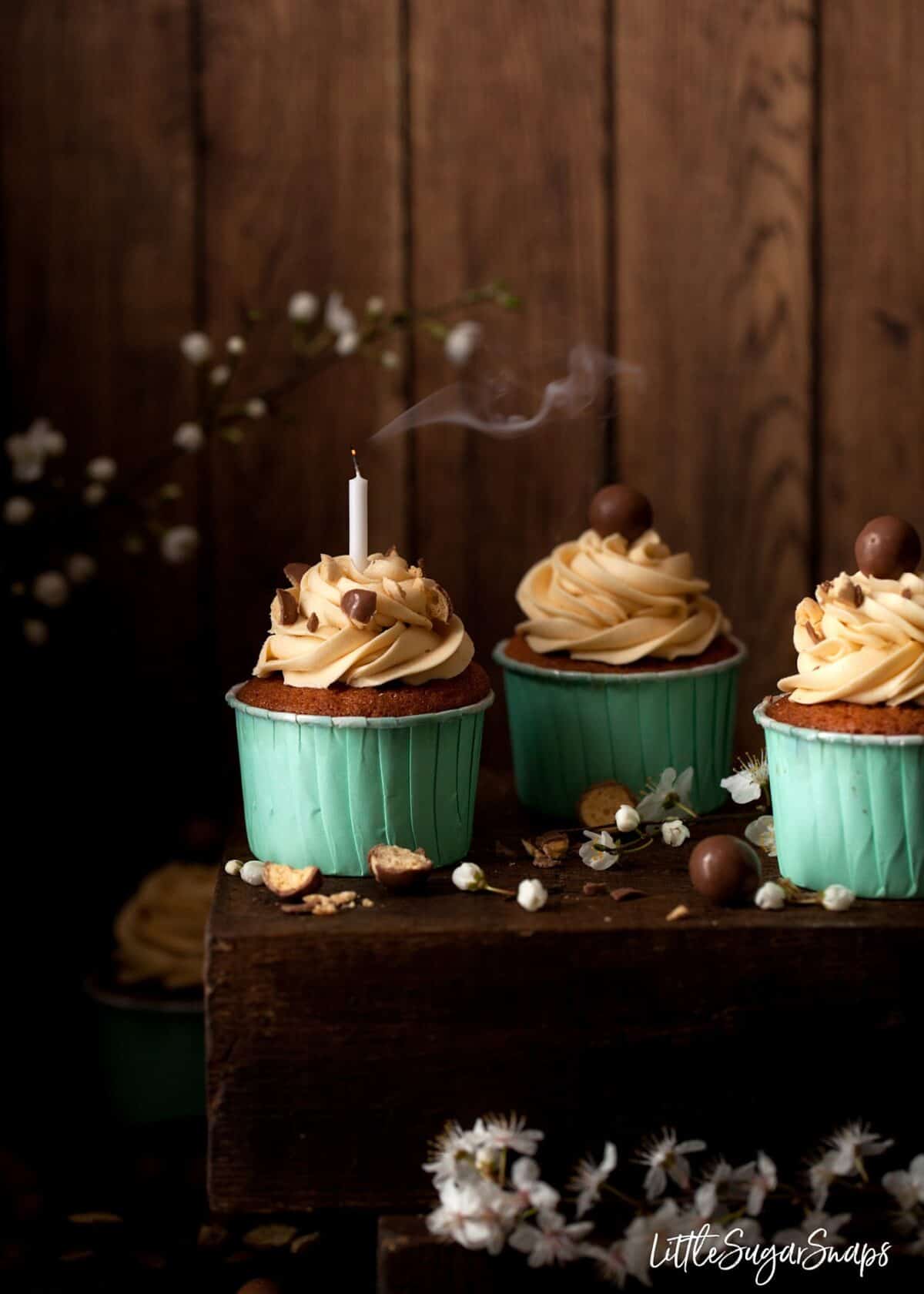 Three small cakes on a wooden board. One with a smoking candle in it.