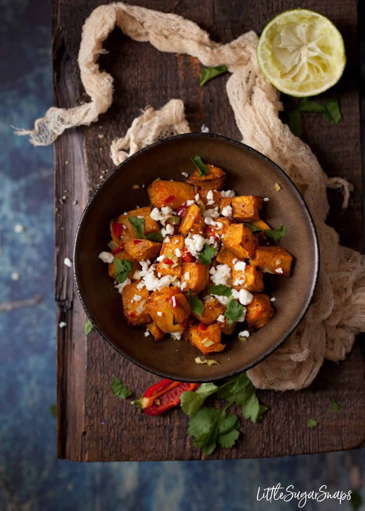 A bowl of roasted sweet potato cubes sprinkled with chilli, onion and feta