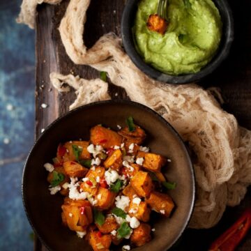 Chilli Feta sweet potatoes in a bowl with a cube being dipped in avocado and feta dip