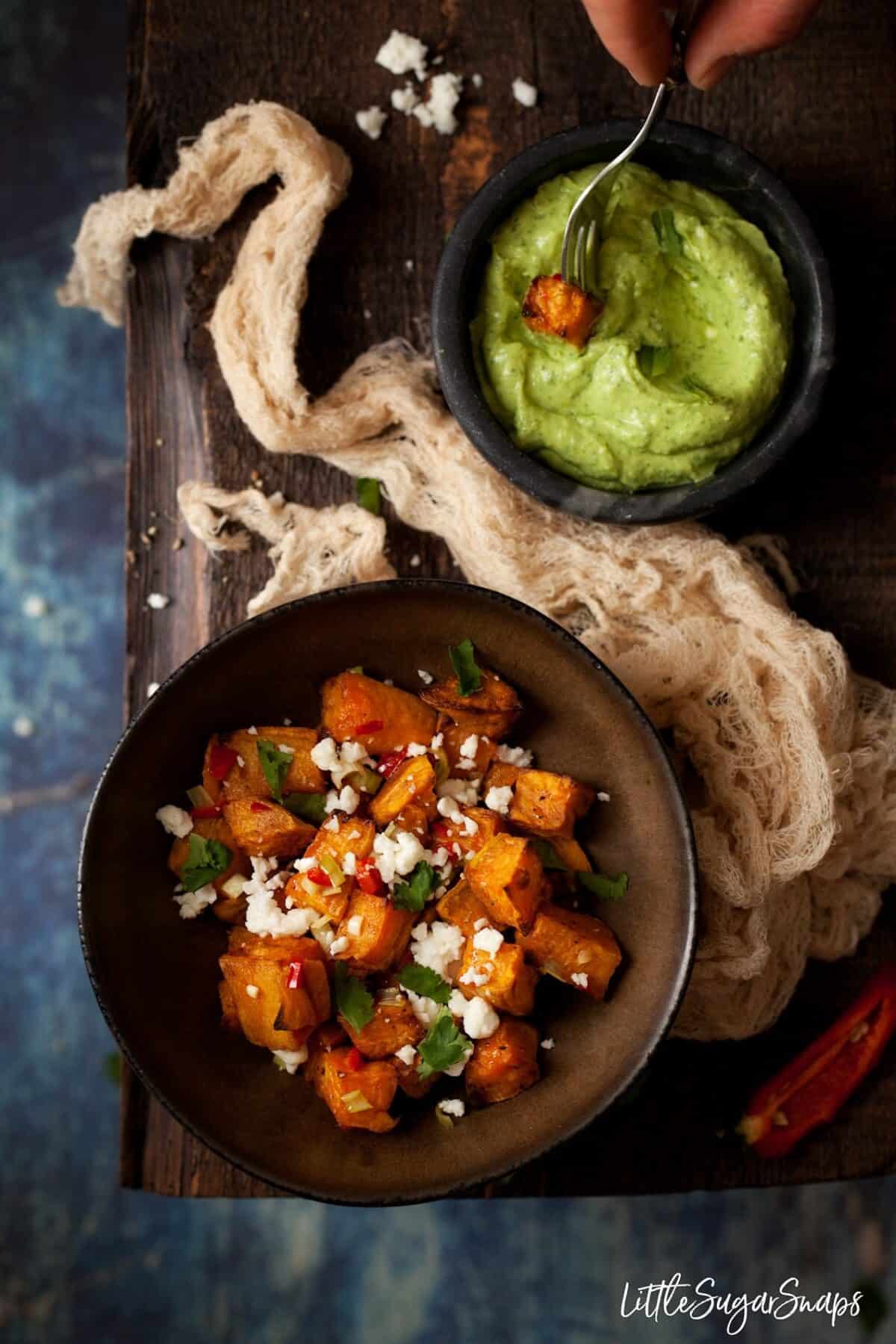 Chilli Feta sweet potatoes in a bowl with a cube being dipped in avocado dip