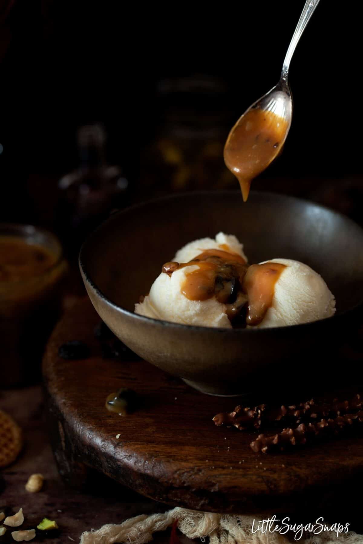 spooning rum & raisin caramel sauce onto vanilla ice cream in a bowl