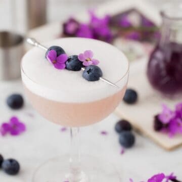 Violet Blueberry Gin Sour garnisged with blueberries and flowers