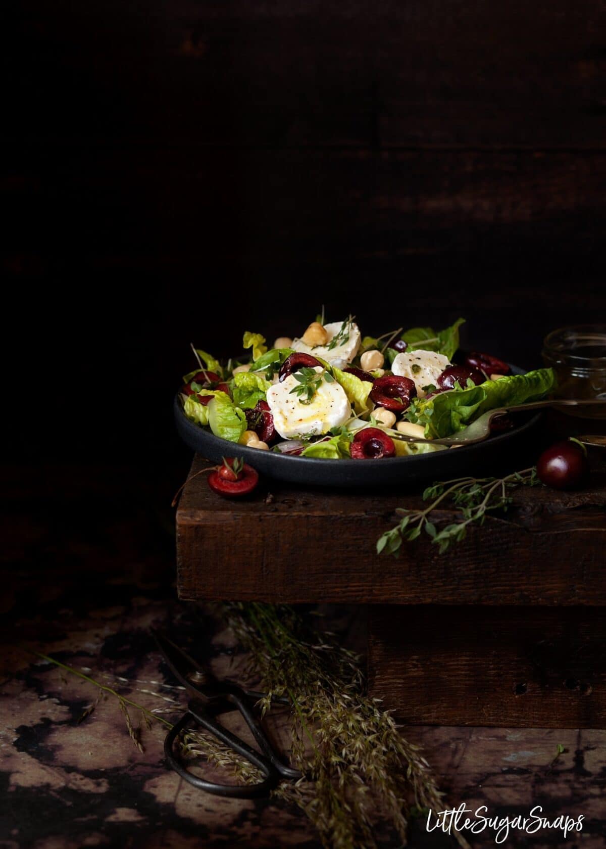 A plate of salad leaves with fresh cherries, goats cheese and thyme.