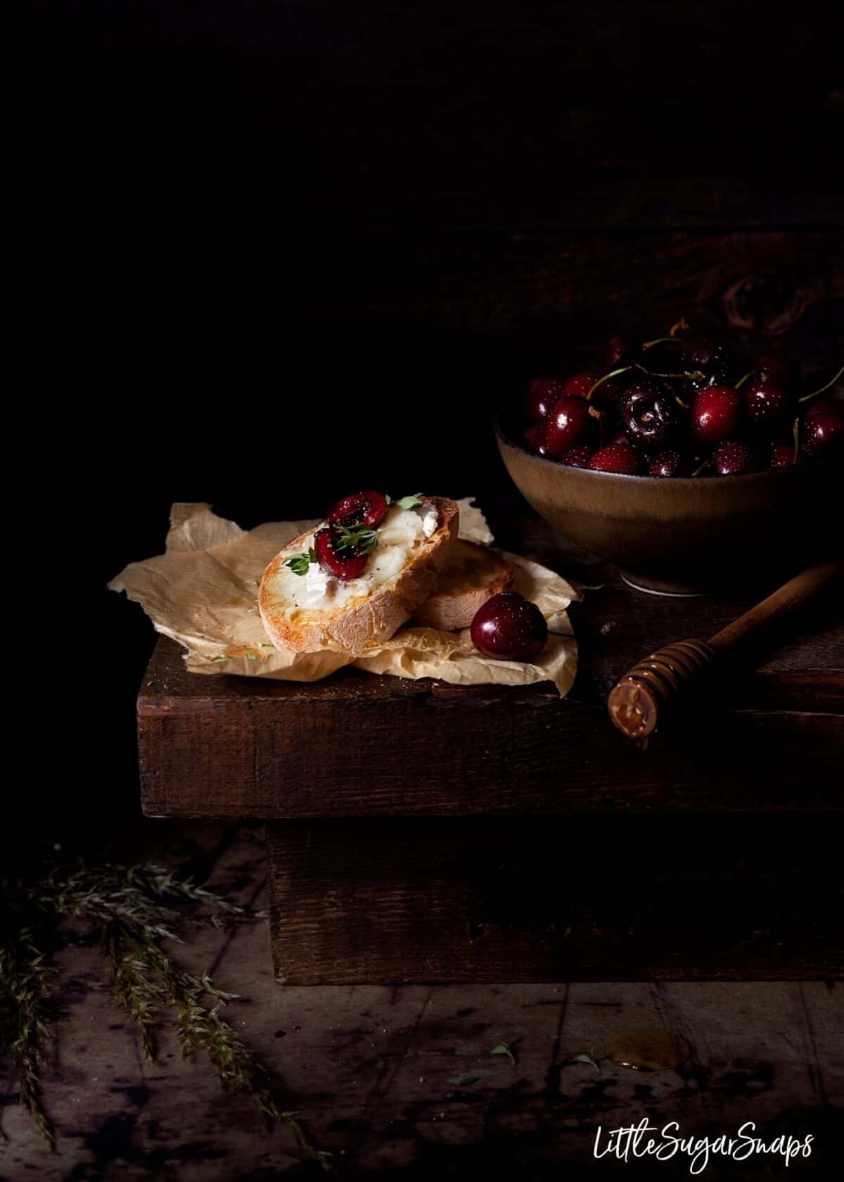 Cherry & goats cheese crostini with honey next to a bowl of cherries.