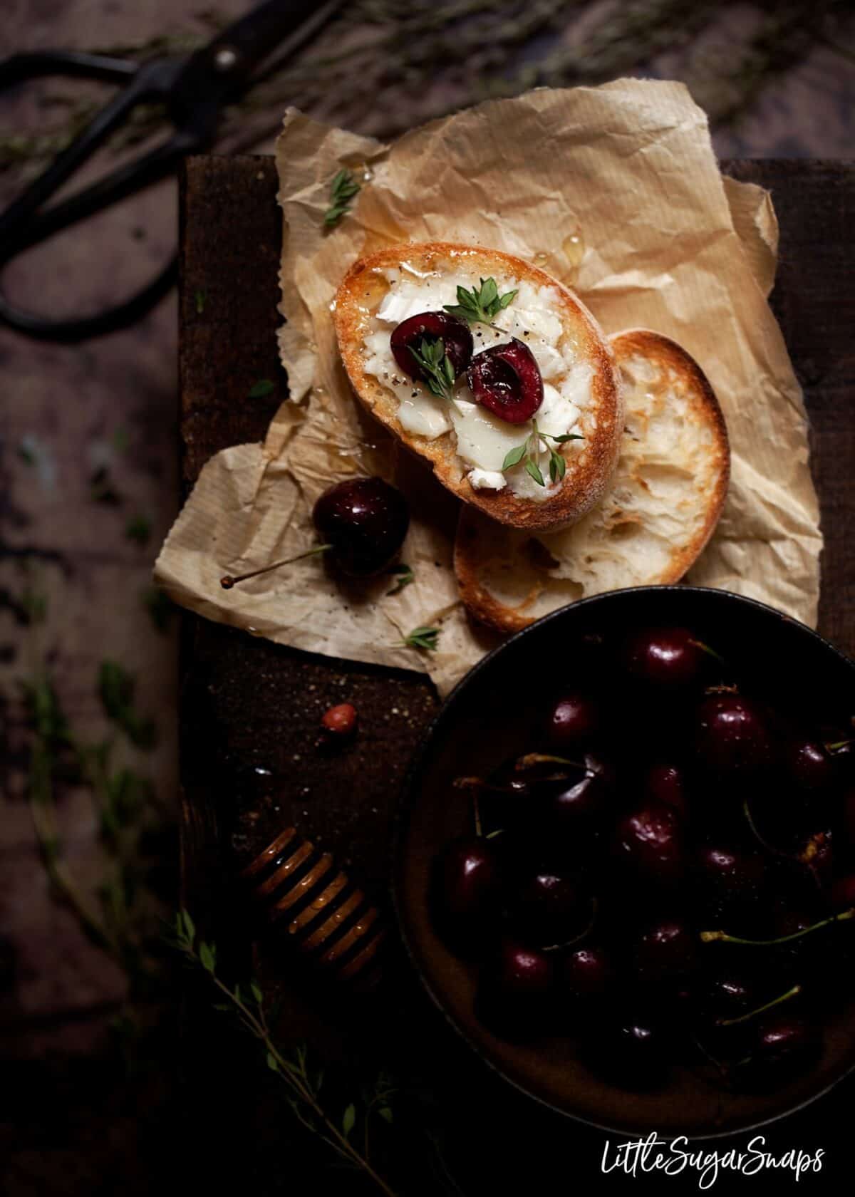 Crostini with goats cheese, cherries and honey next to a bowl of cherries