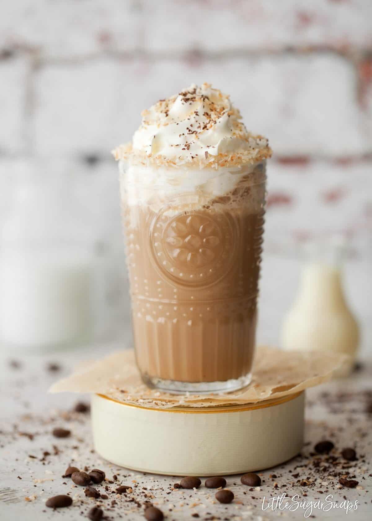 A glass of iced coffee made with coconut milk. With cream and toasted coconut garnish.