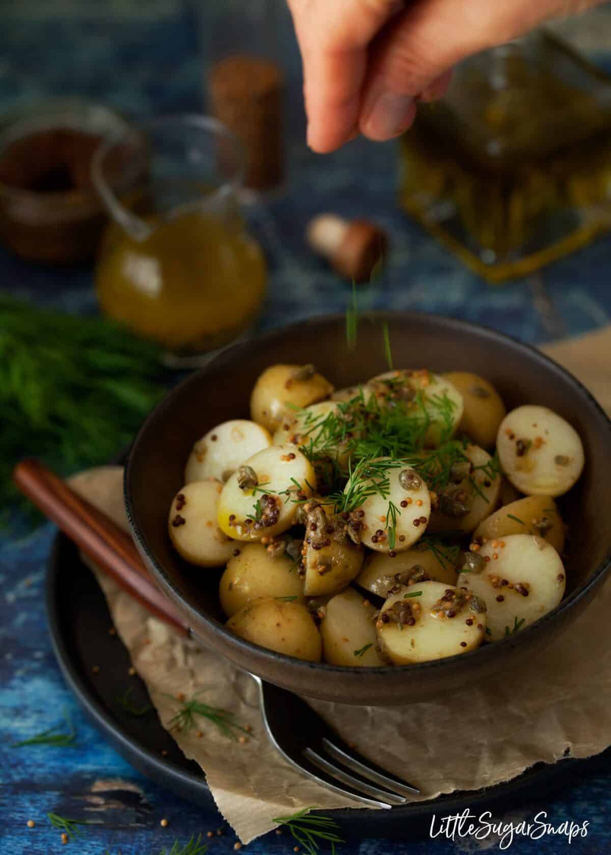 Adding dill to a bowl of potato salad