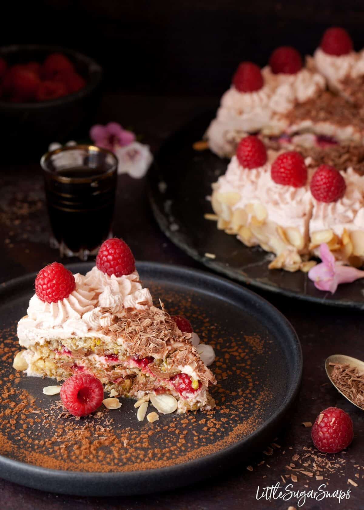 A slice of raspberry dacquoise cake with the rest of the cake behind.