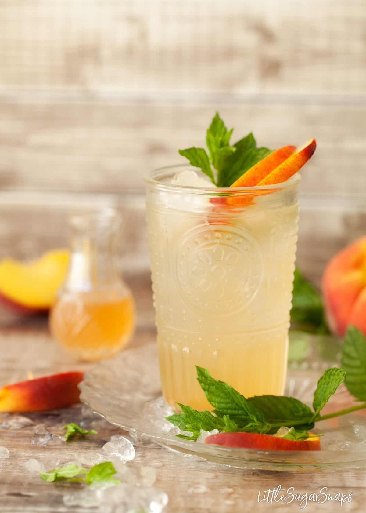 a glass of peach syrup topped up with water with fresh peach and mint