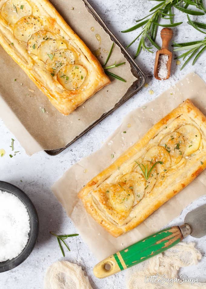 two brie and potato tarts with rosemary and sea salt. Both on baking parchment with ingredients in bowls and around the edges of the image