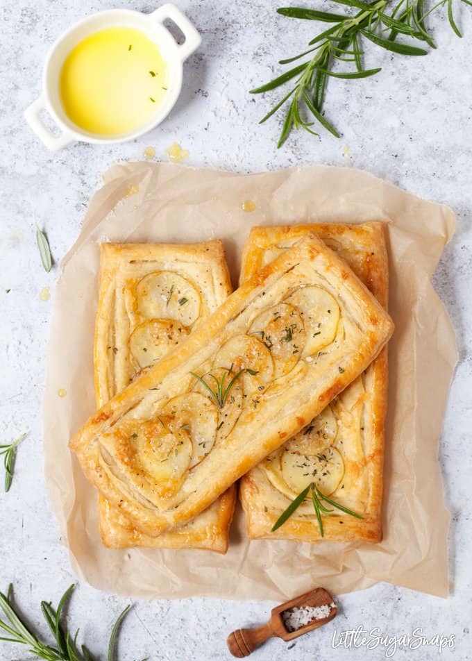 potato tarts on baking parchment with rosemary and sea salt. Olive oil in a bowl and salt on a wooden scoop