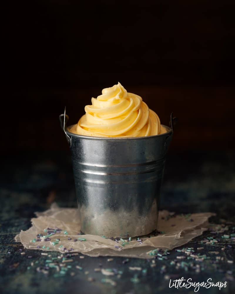 a pot of yellow cake frosting on wax paper with sprinkles scattered around it