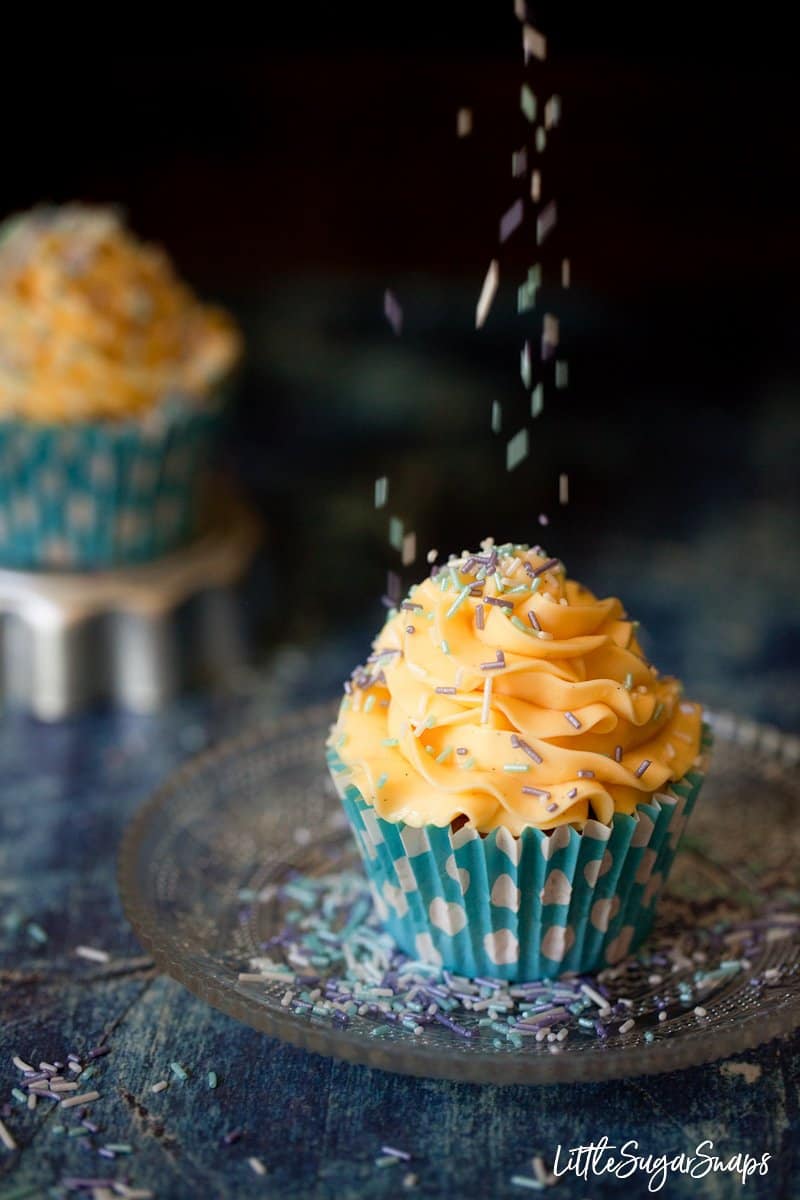 A cupcake topped with vanilla french buttercream with sprinkles being poured on top.