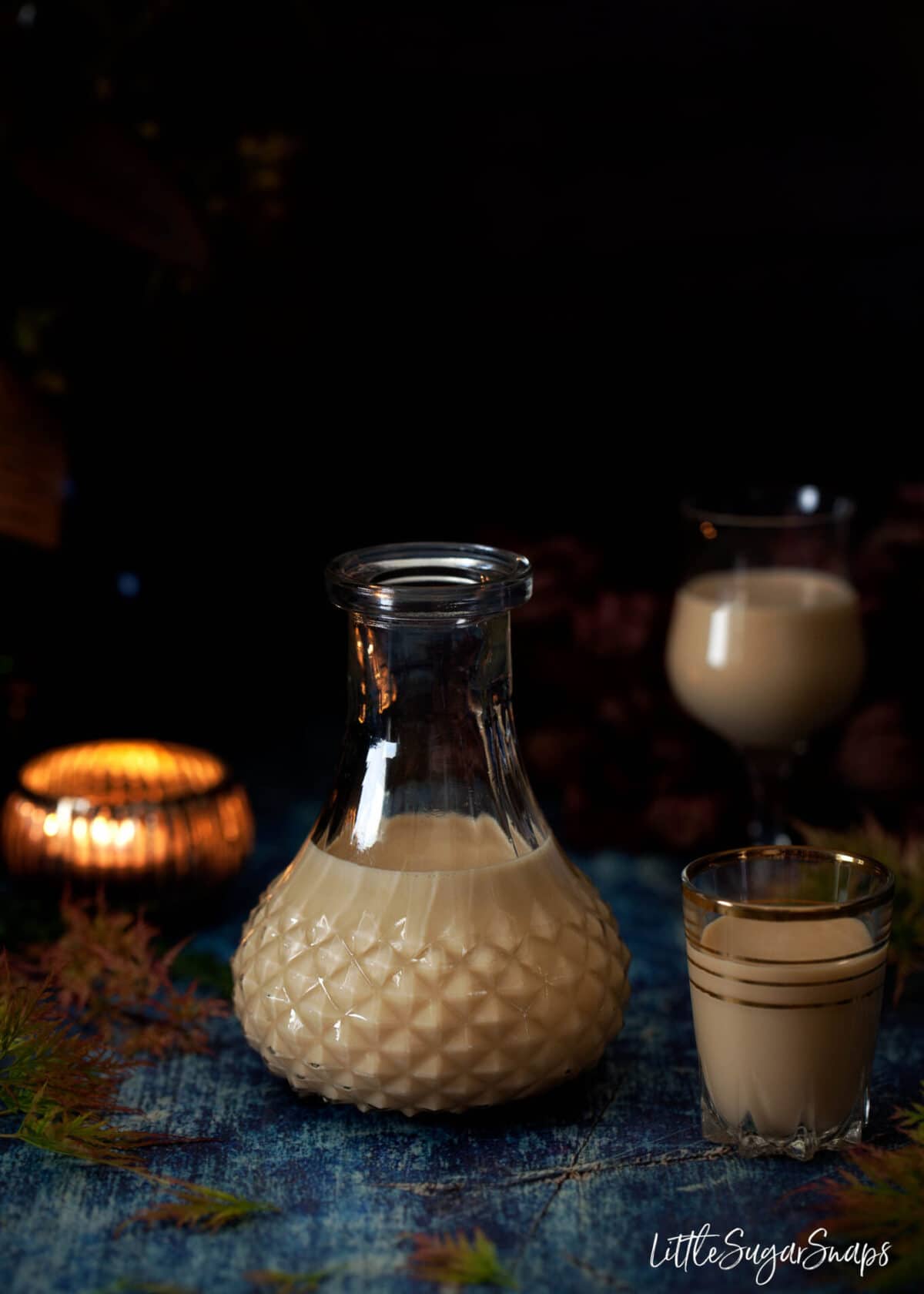 A vintage bottle half filled with creamy caramel liqueur and a shot glass next to it. 