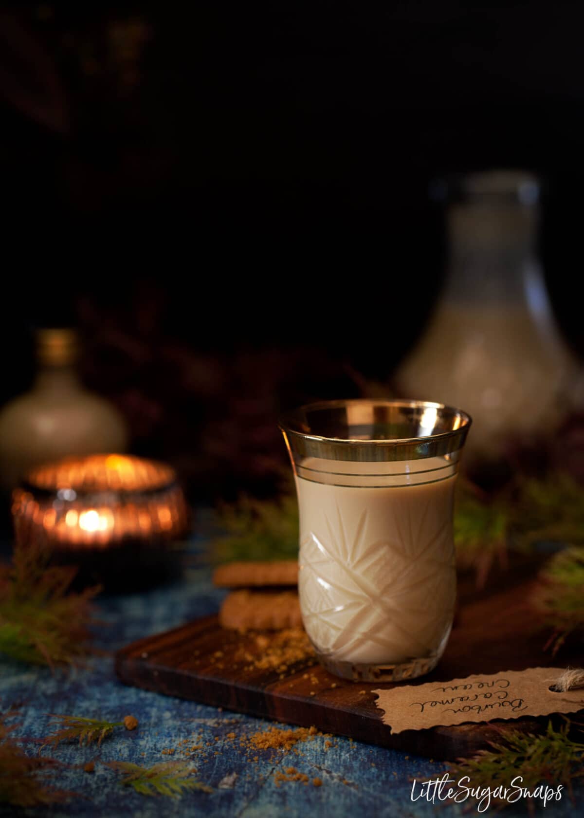 Ornate shot glass of caramel bourbon cream liqueur on a wooden board with a gift tag.