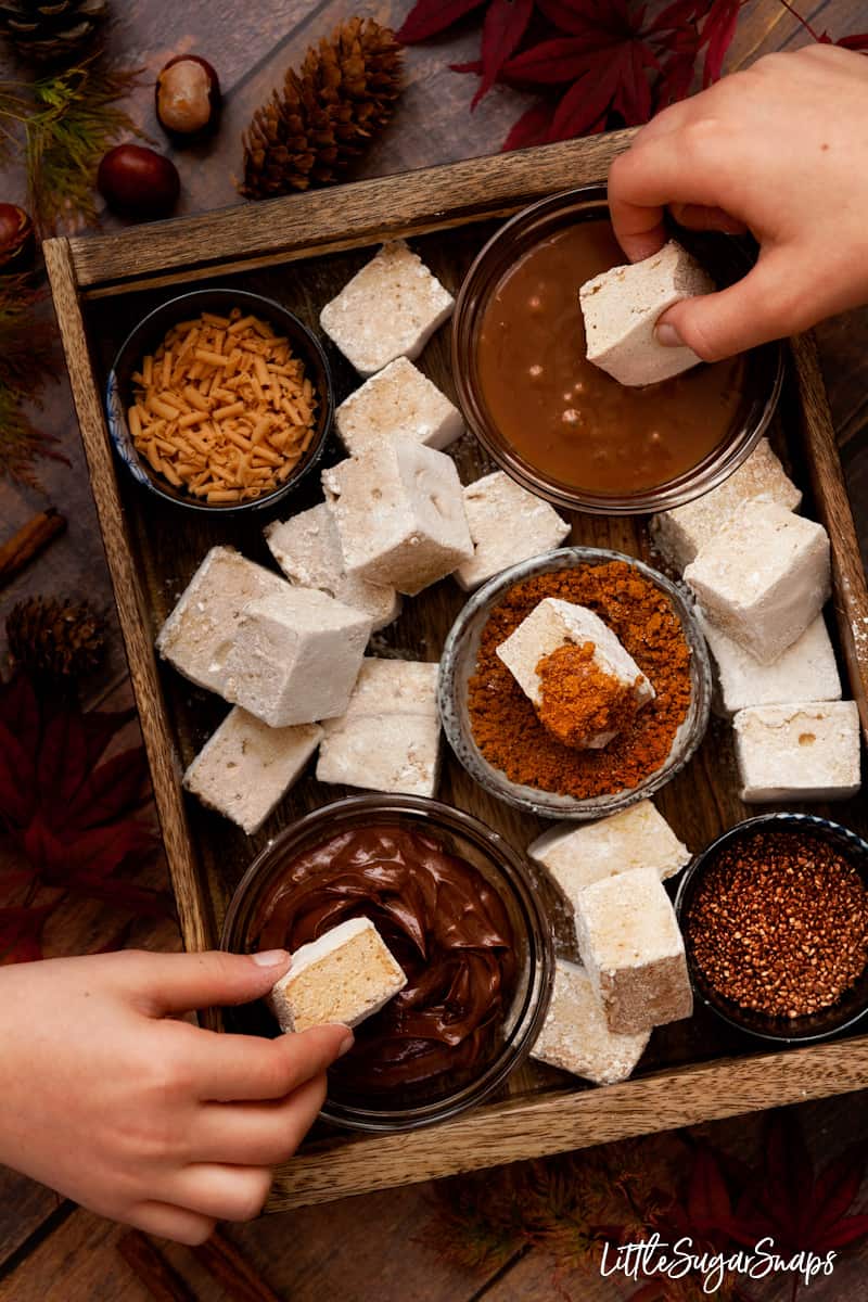 A tray of pumpkin spice marshmallows with children dipping them into sauces and sprinkles.