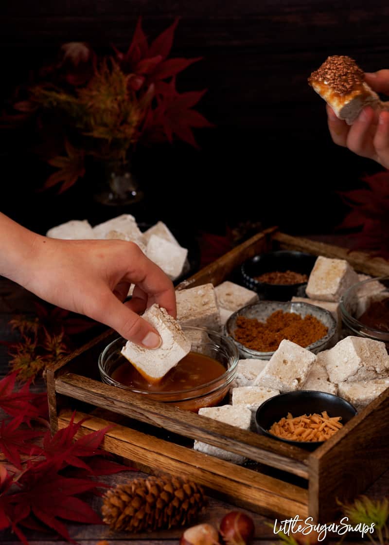 Children dipping chunks of pumpkin spice marshmallow into caramel sauce and various toppings.