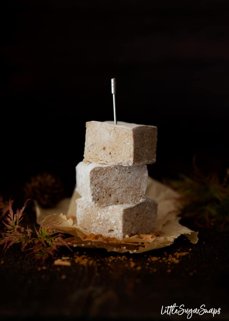 Cubes of homemade marshmallow stacked on greaseproof paper with autumn foliage around it. 