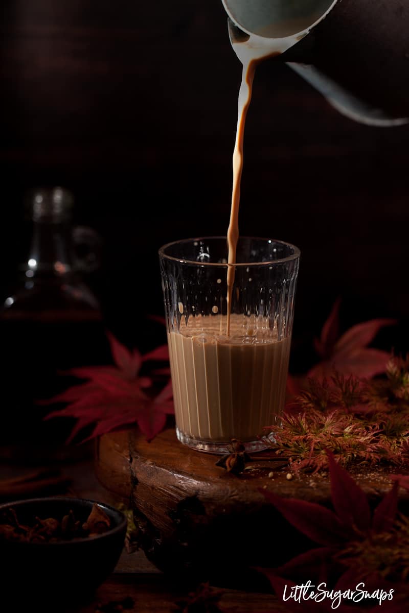 Rum masala chai being poured into a glass with spices alongide. 