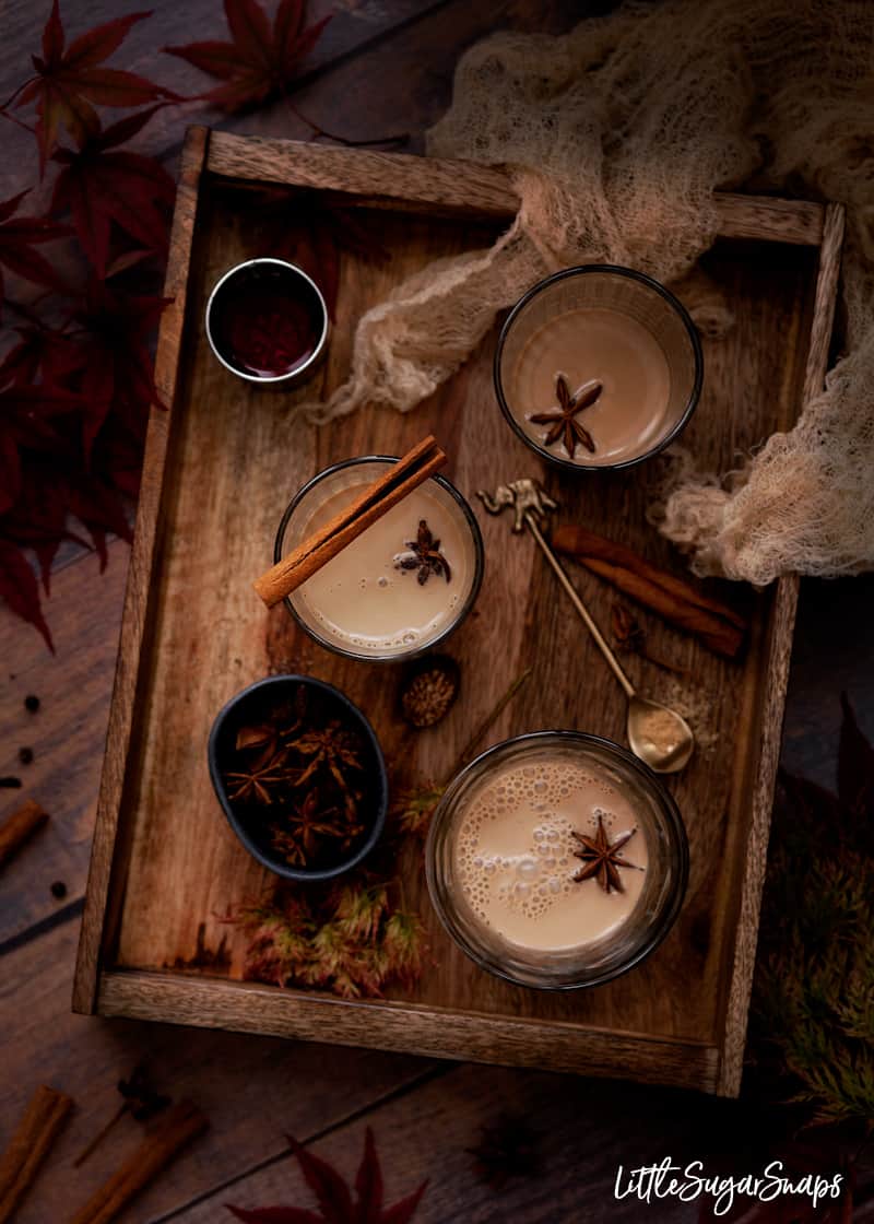 Glasses of spiced tea on a tray with a shot of rum. Whole spices served alongside.