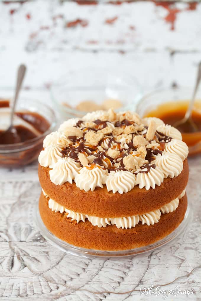 millionaires shortbread cake being decorated with caramel buttercream, caramel & chocolate sauce and crushed cookies. 2 layers of cake and edges are not frosted