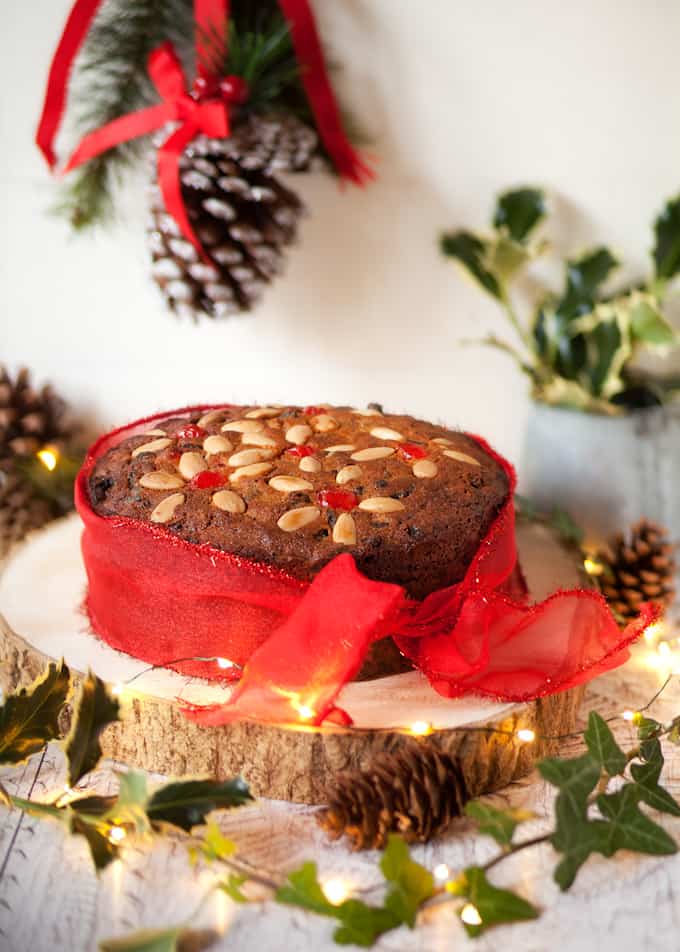 Fruity marzipan cake tied with a red ribbon on a wooden cake board.