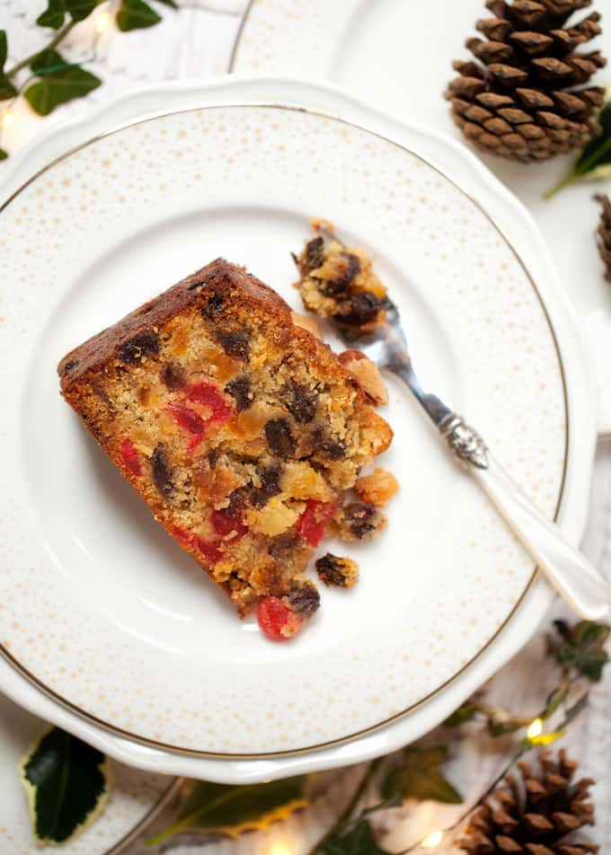 A slice of fruity marzipan cake on a white plate with a dessert fork full of cake

