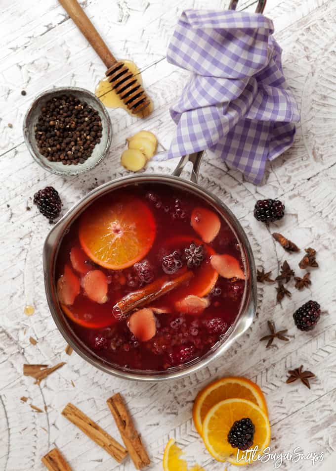 A pan full of mulled apple and blackcurrant juice. It has mulling ingredients like cinnamon and star anise, orange slices and blackberires still in the pan and ingredients scattered around