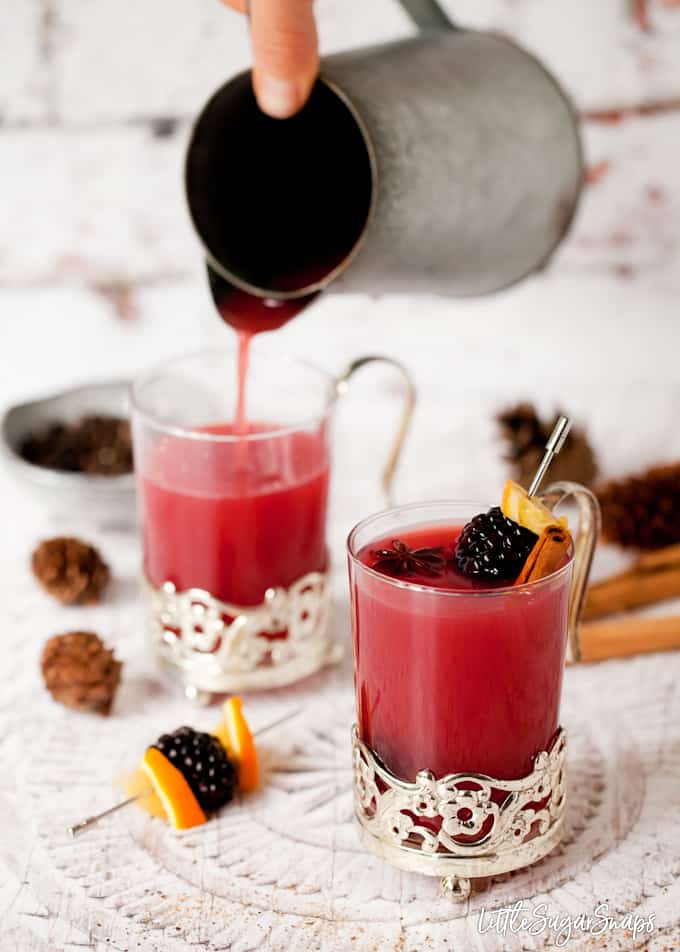 Person pouring hot fruit juice into mugs.