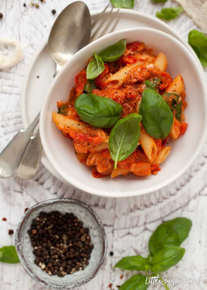 Pasta in a creamy tomato sauce with basil leaves in a white bowl