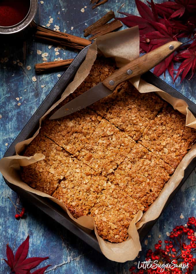 a tin of freshly baked flapjack oat bars cut into squares on a blue background