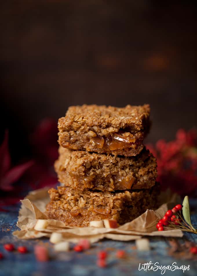 A stack of 3 toffee apple flapjack bars on parchment paper with red foliage in shot